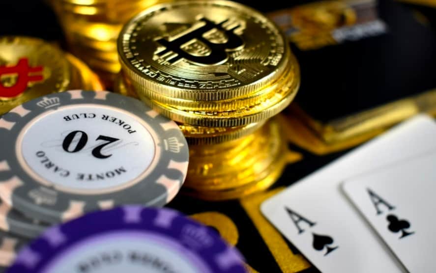 Photo of a stack of poker chips, Bitcoin coins, and playing cards showing two Aces
